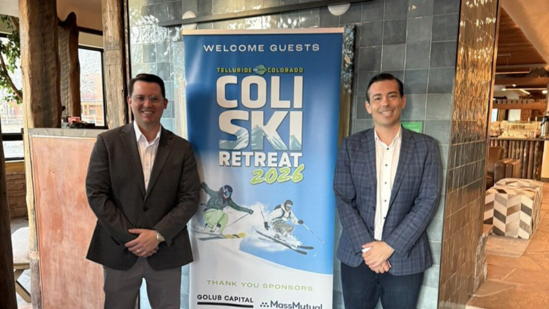 2026-featured-speaker-800x450 Two men standing next to ad for skiing.